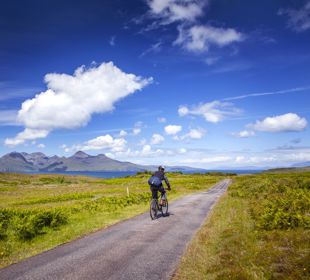 A cyclist going down a single track road with views to other islands in the distance