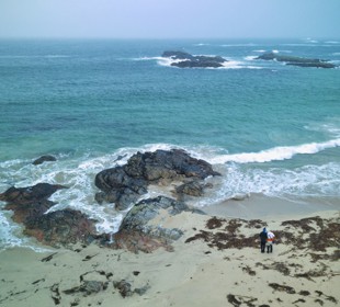 Drone overlooking Straun beach on Coll with the waves crashing against the rocks as a couple look out to sea