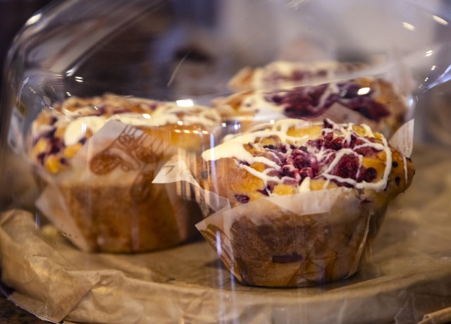 Close-up of iced berry muffins displayed under a clear dome cover on a counter.
