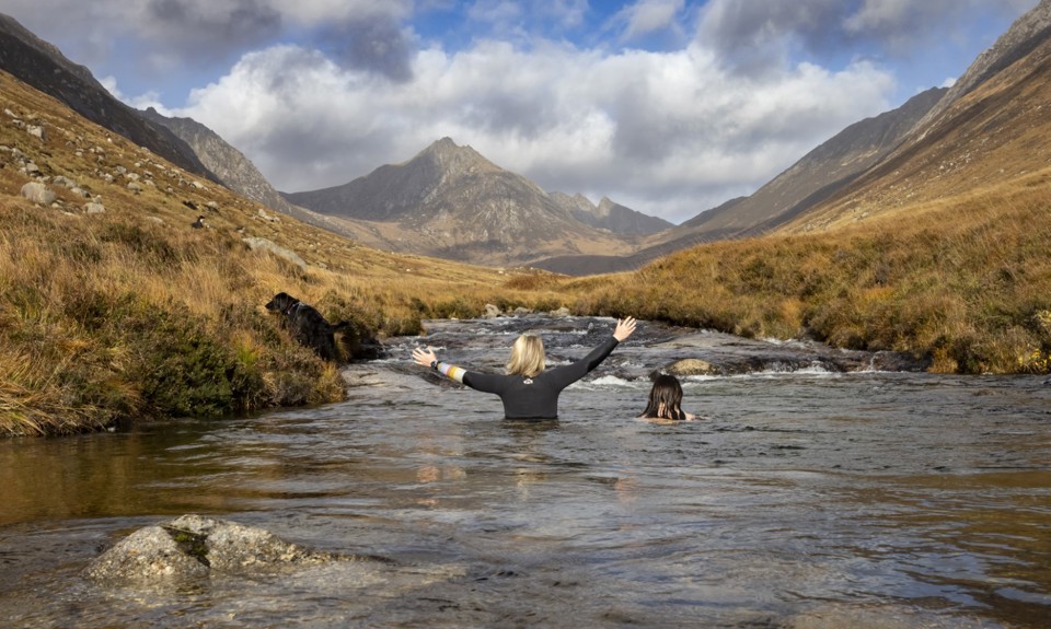 two female swimmers in Glen Rosa (Arran). One has a black wet suit with her hands in the air