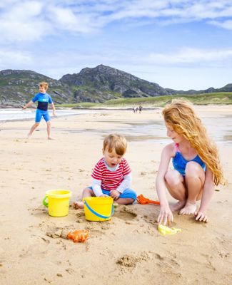 Children at the beach building sandcastles with yellow buckets and spades