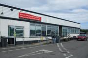 Kennacraig Ferry Terminal with a red bilingual welcome sign in English and Gaelic, accessible parking area, and a red car nearby.