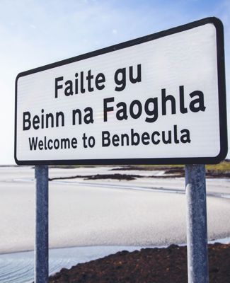 Welcome to Benbecula sign with Gaelic language version, with a white sandy beach in the background.
