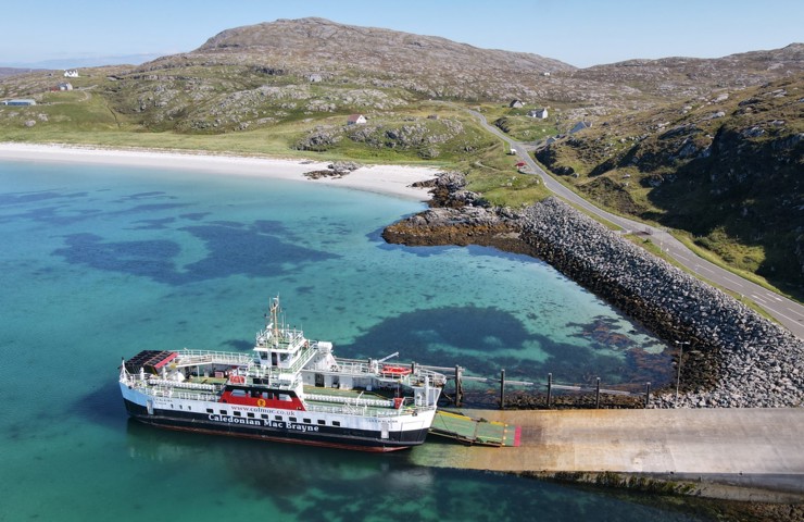 the MV Loch Alainn berthed at Eriskay with the blue water and white sand to the left and the causeway to the right