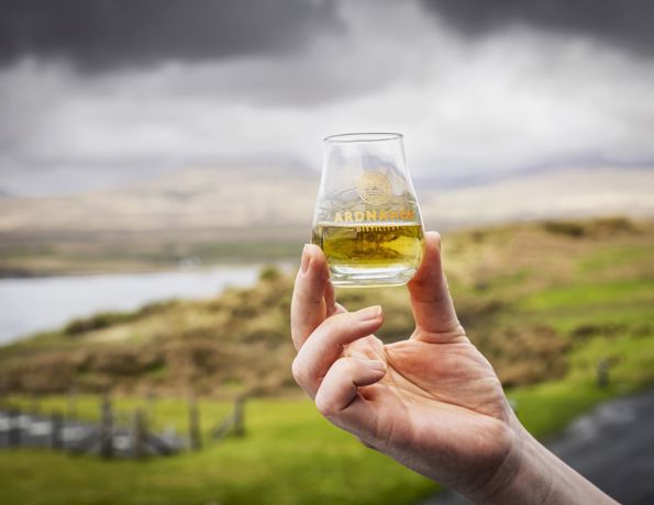 A glass of whisky being held aloft outdoors