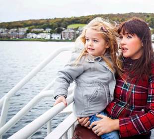 Mother with daughter in her arms looking out to the sea from the outside deck of a ferry