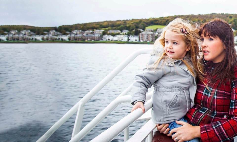 Mother with daughter in her arms looking out to the sea from the outside deck of a ferry